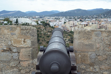 Fototapeta na wymiar Cannon in Ibiza castle, brick walls, city and mountain view. Spain