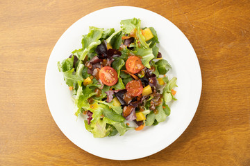 Green garden salad on a white plate on a wooden table