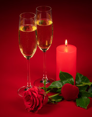 red rose, two glasses of champagne, a lit candle and a red heart on a red background in honor of Valentine's day, wedding day, anniversary