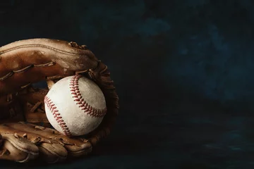 Wall murals Best sellers Sport Moody style baseball background with old ball in leather glove close up for sport, copy space on dark backdrop.