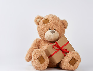 cute big beige teddy bear holds a brown box with a red ribbon