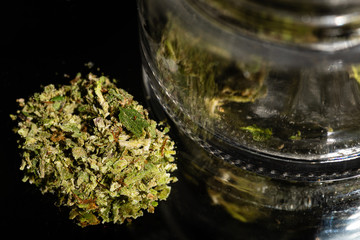 A small amount of ground up marijuana near a Jar of buds, ready to be burned in a pipe or rolled in a joint.