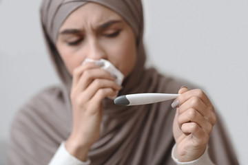Sick arabic woman in headscarf holding thermometer and blowing runny nose
