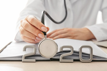 Female doctor with stethoscope, notebook and figure 2020 on table, closeup