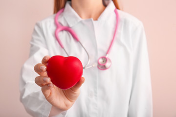 Female cardiologist with red heart on color background, closeup