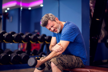 Man feeling strong elbow pain while training with dumbbells in the gym. People, fitness and...