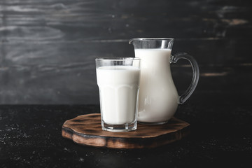 Glass and jug of tasty milk on dark table