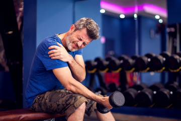 Man feeling strong shoulder pain while training with dumbbells in the gym. People, fitness and healthcare concept