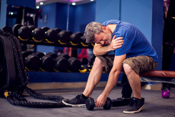 Fototapeta na wymiar Man feeling strong shoulder pain while training with dumbbells in the gym. People, fitness and healthcare concept