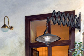 friction pantograph pendant electric heater mounted on the light wall of the street cafe with a brown window, black heater in the loft style close up.