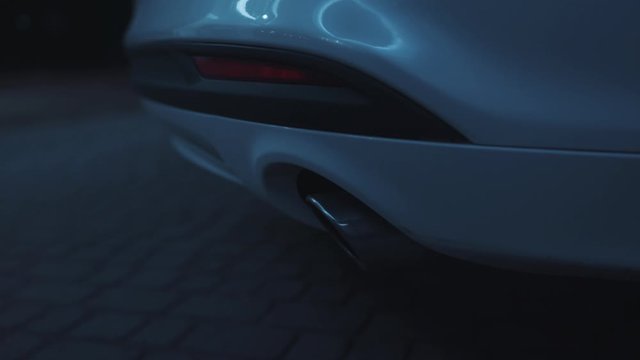 Low angle view on white sports modern car exhaust. Close-up luxury back of car with tailpipe polluting air with smoke with sound of motor rattle.