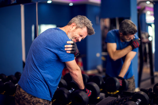 Man feeling strong shoulder pain while training with dumbbells in the gym. People, fitness and healthcare concept