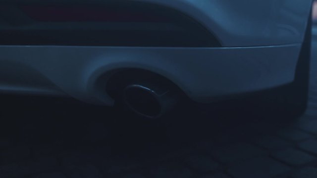 Smoke emission from modern car tailpipe close-up. Low angle shot of luxurious new white automobile exhaust pipe polluting air. Car details.