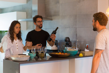 Smiling young friends preparing wine for tasting. Group of cheerful people standing near table and talking. Wine tasting concept