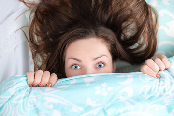 Amazing girl with open eyes looking out from under the covers