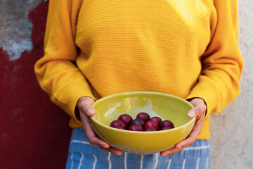 Unrecognizable woman holding up a bowl with plumps fruit