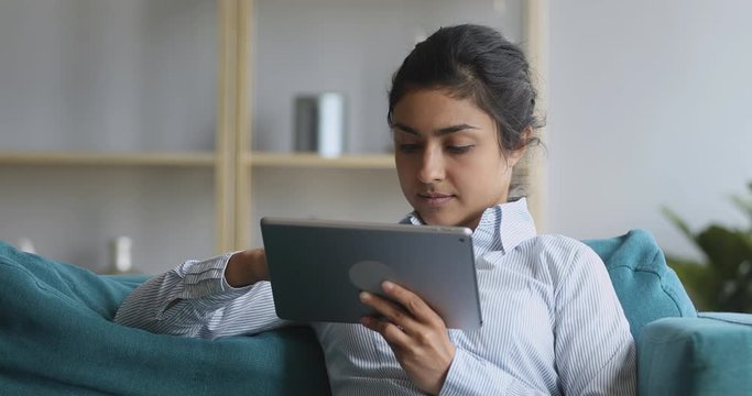 Indian woman relaxing at home on couch using digital tablet