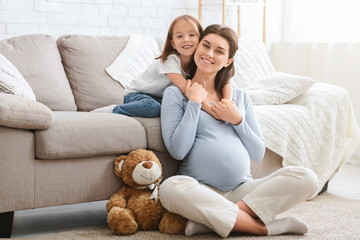 Smiling little daughter hugging her happy pregnant mom