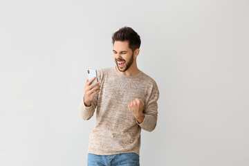 Happy young man with mobile phone on grey background