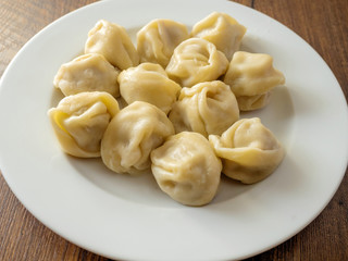 Portion of traditional Russian cooked dumplings on a white plate and wooden table,