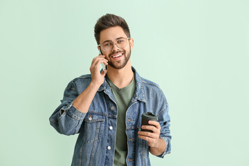 Happy young man talking by mobile phone on color background
