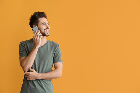 Happy Young Man Talking By Mobile Phone On Color Background