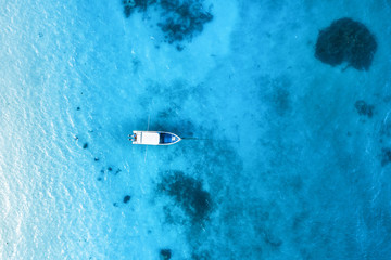 Aerial view of the white boat in the clear blue water at sunset in summer. Top view from drone of yacht, sandy beach in Indian ocean. Travel in Zanzibar, Africa. Tropical landscape with motorboat, sea