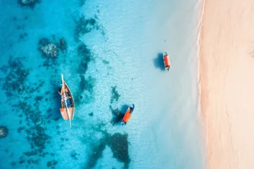 Poster Luchtfoto van de vissersboten in helder blauw water bij zonsondergang in de zomer. Bovenaanzicht van drone van boot, jacht, zandstrand in Zanzibar. Reis. Tropisch zeegezicht met zeilboten, zee. Uitzicht van boven © den-belitsky