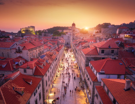 Fototapeta Aerial view of beautiful old city at sunset. Top view of houses with red roofs, city lights, historical centre, architecture, walking people in illuminated streets at night in Dubrovnik, Croatia