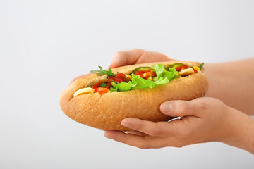 Female hands with tasty hot dog on light background