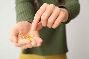 Young woman with fish oil on light background, closeup