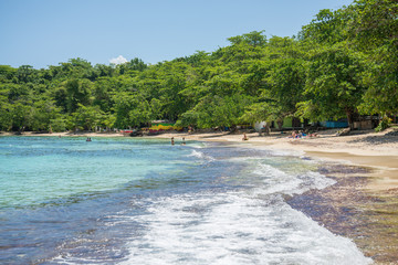 Shore of Winnifred Beach, Jamaica. Turquoise waters, little waves and ripples. Blue sky and green trees in the background