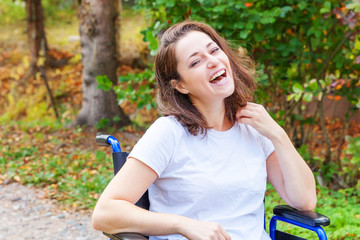 Young happy handicap woman in wheelchair on road in hospital park enjoying freedom. Paralyzed girl...