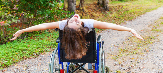Young happy handicap woman in wheelchair on road in hospital park enjoying freedom. Paralyzed girl...