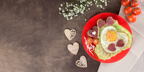 Tasty healthy breakfast concept. Fried scrambled eggs heart-shaped on a red plate with sausages chorizo salami in the shape of a heart and fresh vegetables with sause. Top view, banner, flatlay