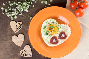 Tasty healthy breakfast for Valentine's Day and Mother's Day. Fried scrambled eggs heart-shaped on an orange plate with sausages chorizo salami in the shape of a heart with fresh herbs. Homemade food