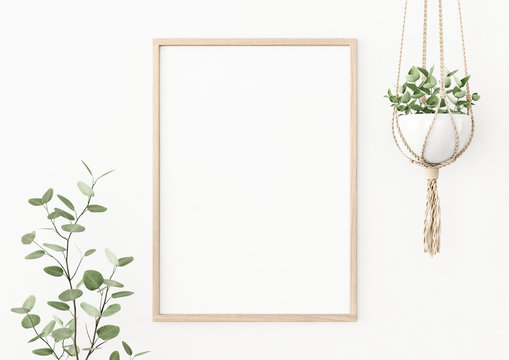 Interior poster mockup with vertical wooden frame on empty white wall decorated with plant branch and hanging macrame pot. A4, A3 size format. 3D rendering, illustration.