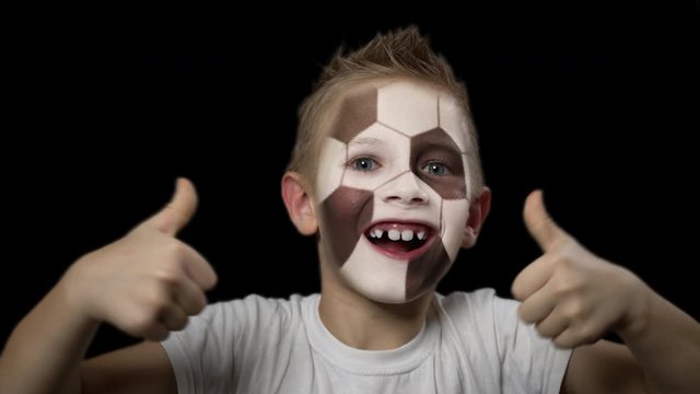 Happy boy rejoices victory of his favorite team. A child with a face painted as football ball. Portrait of a happy young fan. Joyful emotions and gestures. Victory. Triumph.