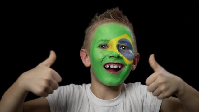 Happy boy rejoices victory of his favorite team of Brazil. A child with a face painted in national colors. Portrait of a happy young fan. Joyful emotions and gestures. Victory. Triumph.