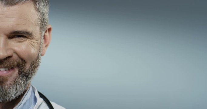 Close up of the half face of the cheerful Caucasian man doctor with a beard smiling and looking straight to the camera. Portrait.