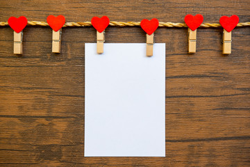 Red heart hanging on the clothesline , paper card on wood background