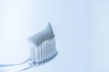 Transparent plastic toothbrush with white toothpaste on a blue white background with reflection on...