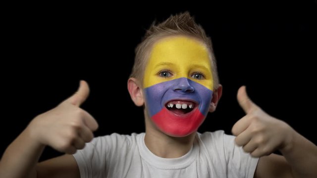 Happy boy rejoices victory of his favorite team of Columbia. A child with a face painted in national colors. Portrait of a happy young fan. Joyful emotions and gestures. Victory. Triumph.