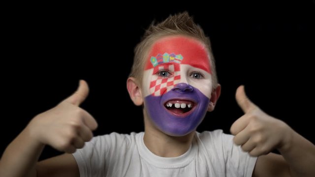 Happy boy rejoices victory of his favorite team of Croatia. A child with a face painted in national colors. Portrait of a happy young fan. Joyful emotions and gestures. Victory. Triumph.
