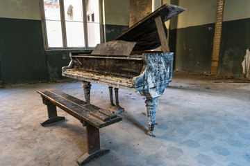 Old dirty black piano with a brown bench in an empty abandoned room - large windows and green walls