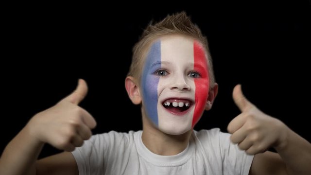 Happy boy rejoices victory of his favorite team of France. A child with a face painted in national colors. Portrait of a happy young fan. Joyful emotions and gestures. Victory. Triumph.