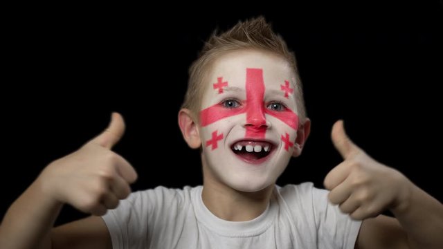 Happy boy rejoices victory of his favorite team of Georgia. A child with a face painted in national colors. Portrait of a happy young fan. Joyful emotions and gestures. Victory. Triumph.