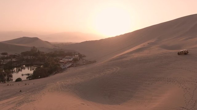 Sandy desert oasis lake. DRONE.  Tourism shot in Huacachina, Peru. Water in middle of hot sand desert. Adventure Dune Buggy, Speed. Epic, Fast. Romantic, holiday, honeymoon, scenic shot.
