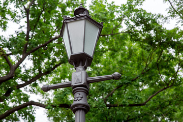 retro style iron lantern with glass inserts and design elements in the park in the background trees on a summer day.