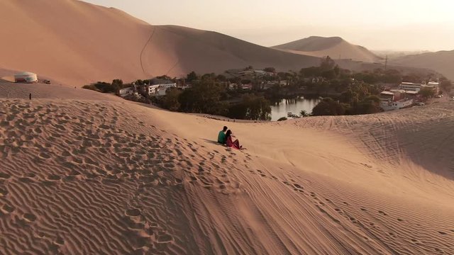 Couple in Sandy desert oasis lake. DRONE. Tourism shot in Huacachina, Peru. Romantic, holiday, honeymoon, scenic shot.Water in middle of hot sand desert. Adventure Dune Buggy, Speed. Epic, Fast. 